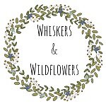 Illustrated Whiskers & Wildflowers logo, with floral wreath.